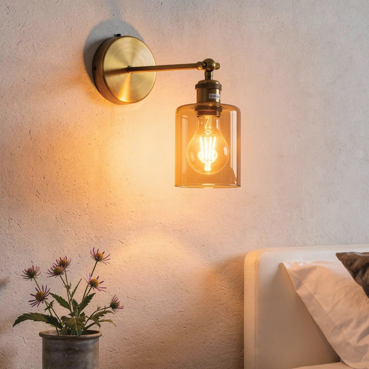 Vintage brass wall sconce with adjustable swing arm and amber glass cylinder shade mounted on a white wall