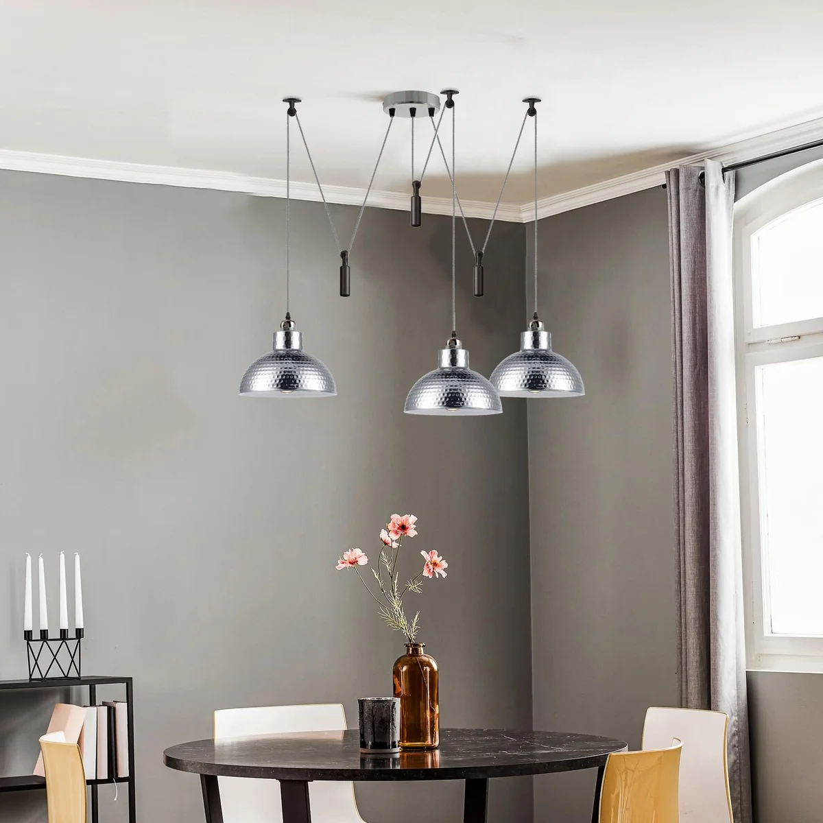 Three vintage ceiling lights with oxidized metal finish hanging at staggered heights over a dining table on adjustable cables