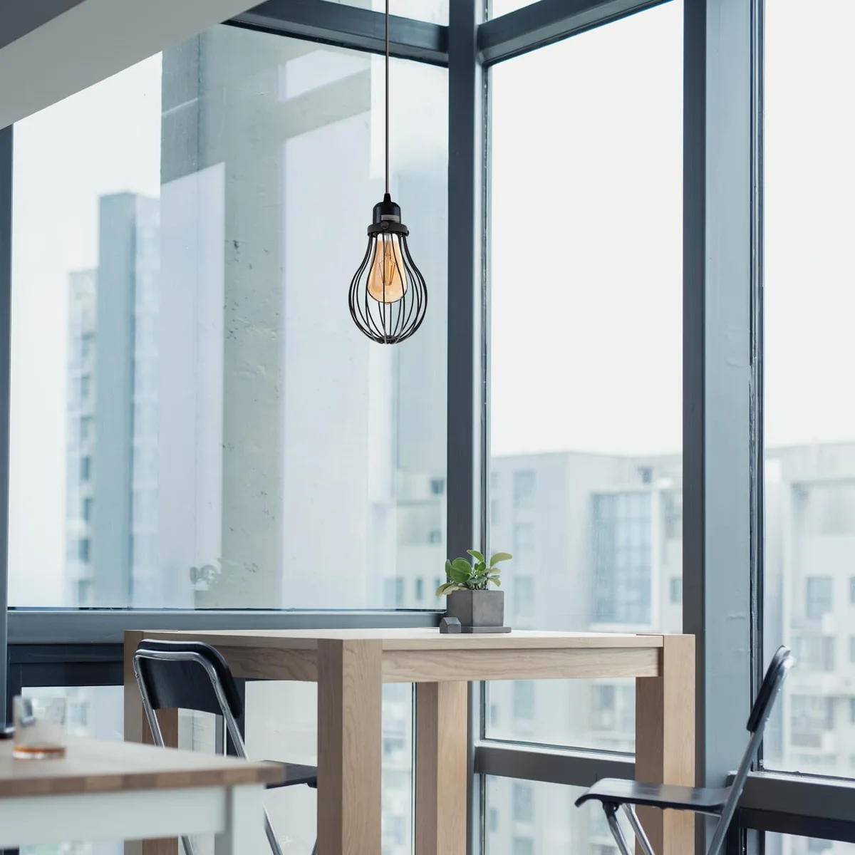 Adjustable vintage industrial pendant lighting with black and French gold wire cage and E27 bulb over wooden table