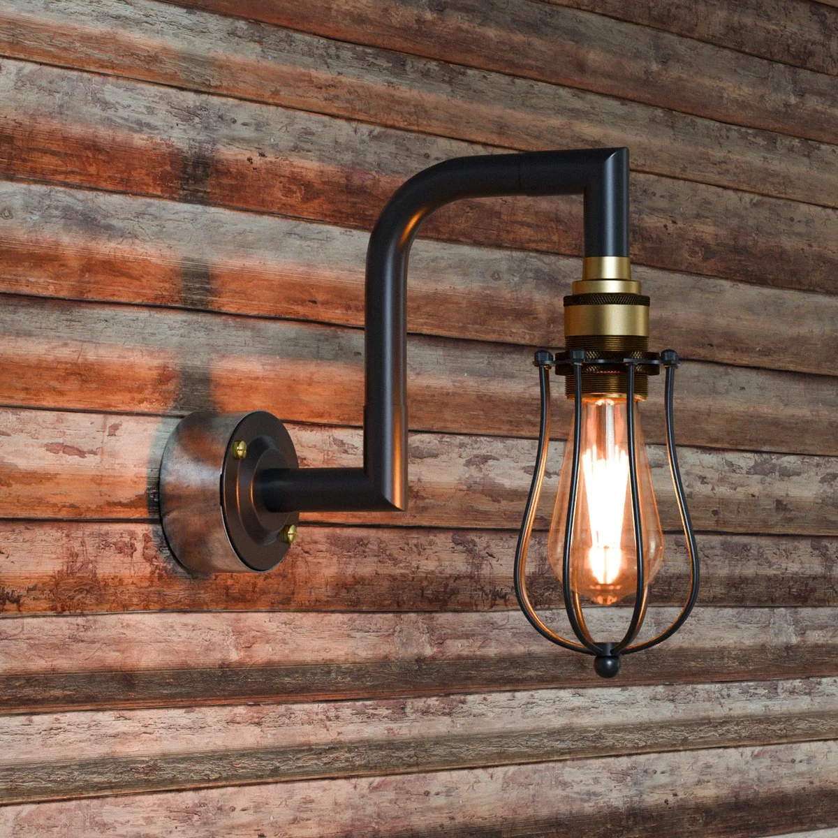 Black brass industrial pipe wall light with vintage metal cage design mounted on a white wall, E27 bulb base visible