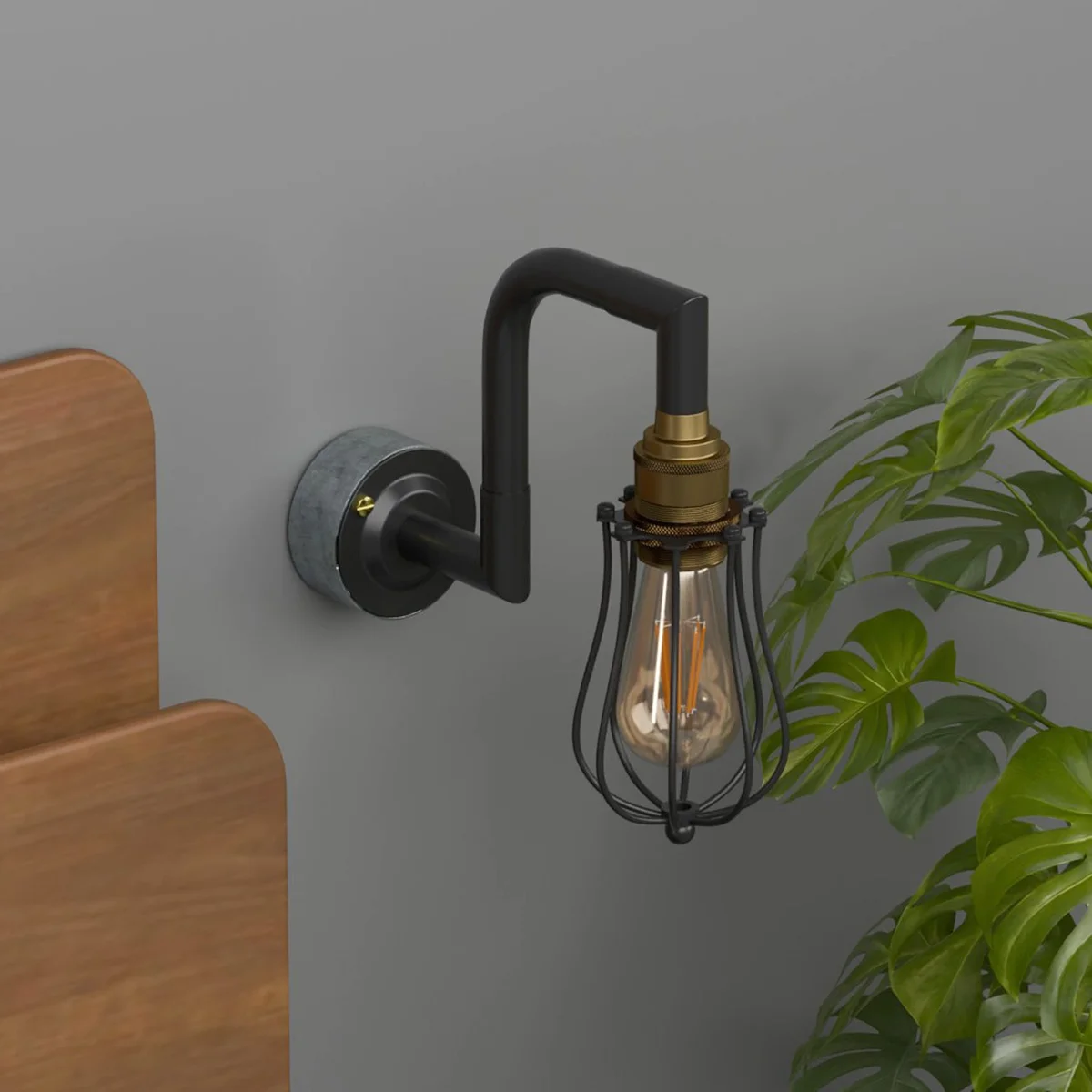 Black brass industrial pipe wall light with vintage metal cage and matte finish, shown mounted on a wall indoors