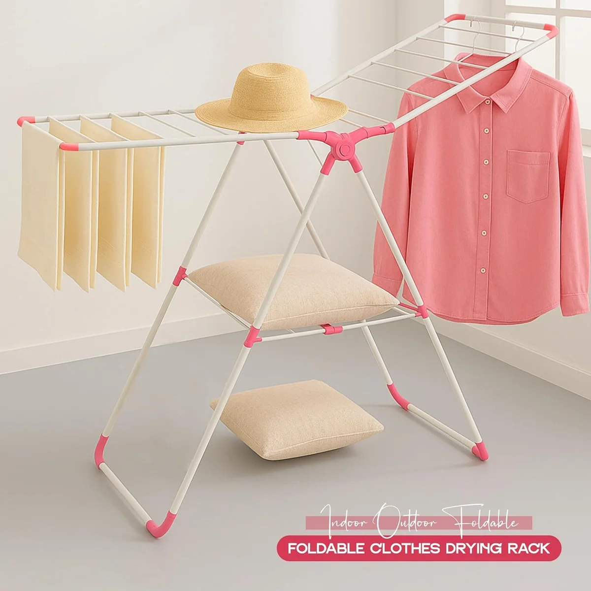Foldable clothes drying rack with three-tier stainless steel frame, white and pink, shown fully extended indoors with laundry hanging