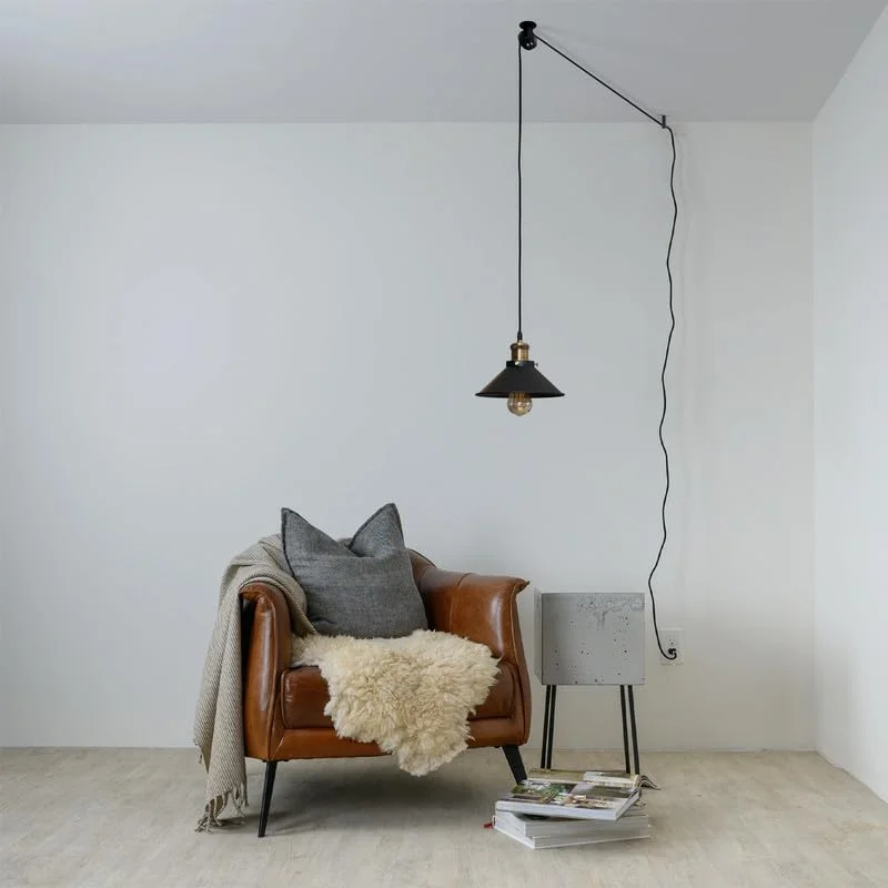 Black adjustable pendant light pulley wheel system mounted on wall with metal frame and mounting screws visible