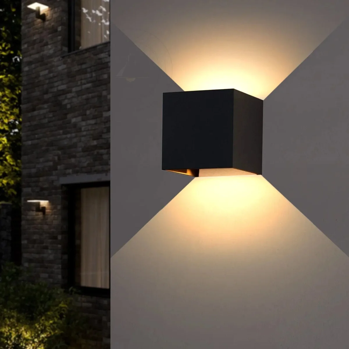Two black square outdoor LED wall lights with motion sensors mounted on a white wall, casting warm white light up and down