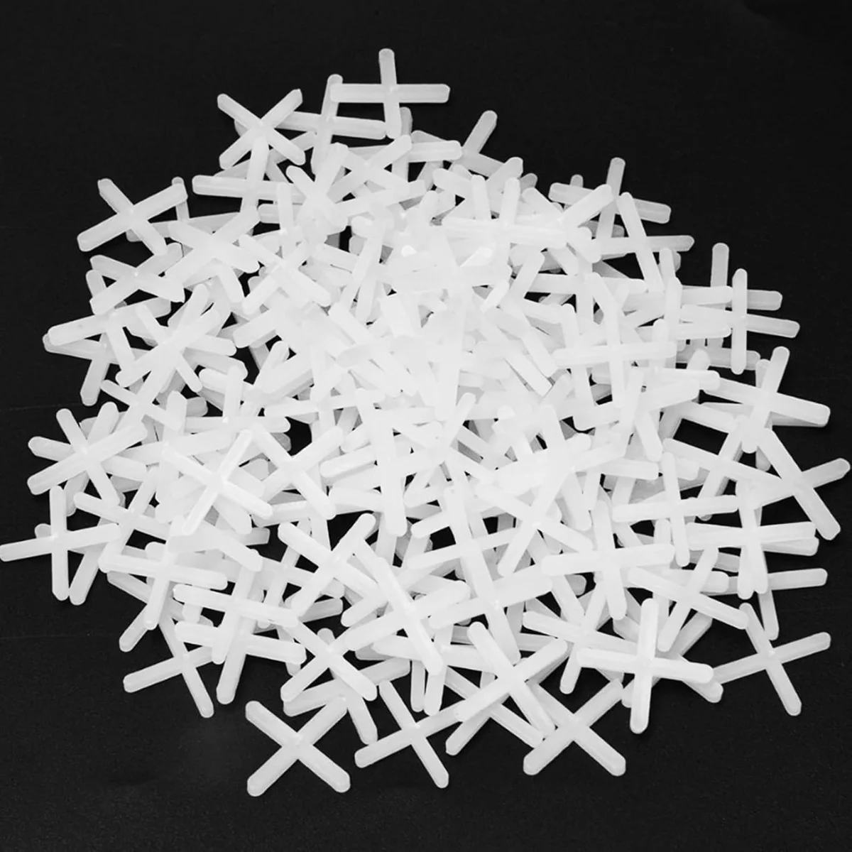 White plastic tile spacers shaped like crosses, arranged in a pile on a plain background