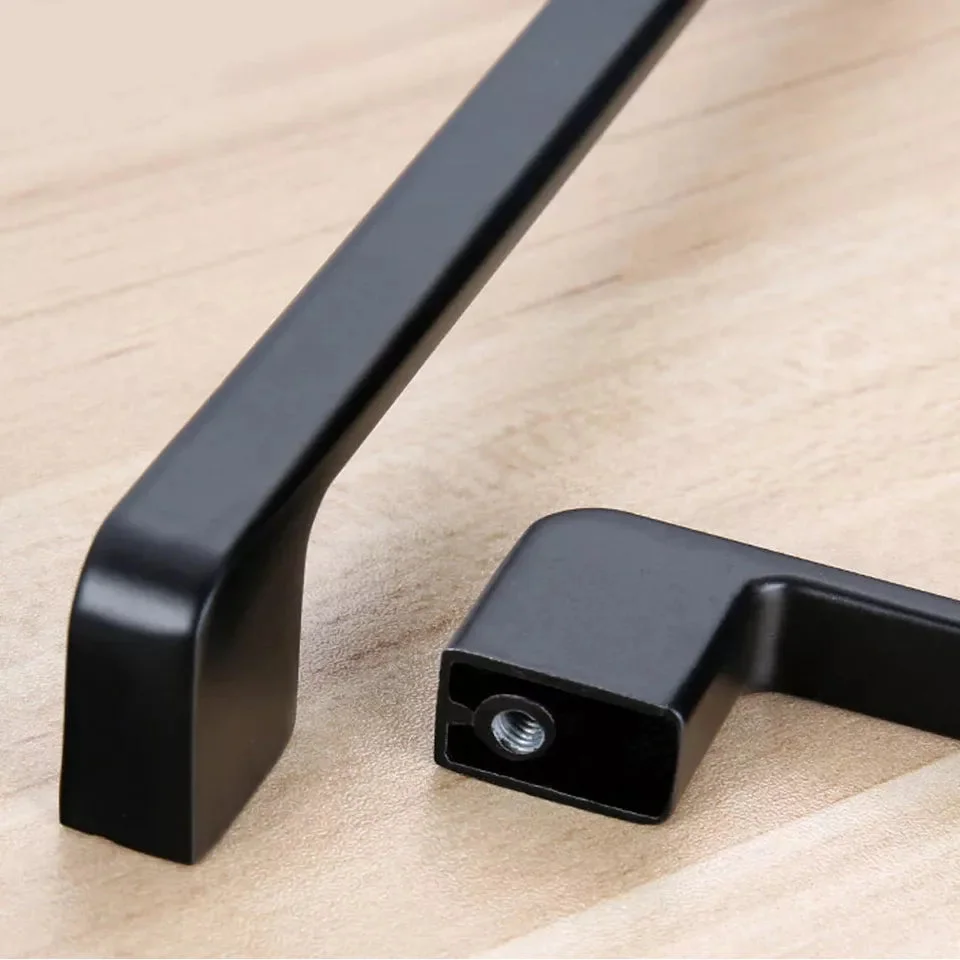 Vintage metal door handle in matte black finish mounted on wooden kitchen cupboard cabinet door