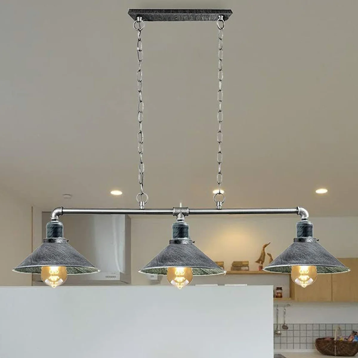 Brushed silver 3‑bulb pendant light with metal pipe design hanging over a kitchen table.