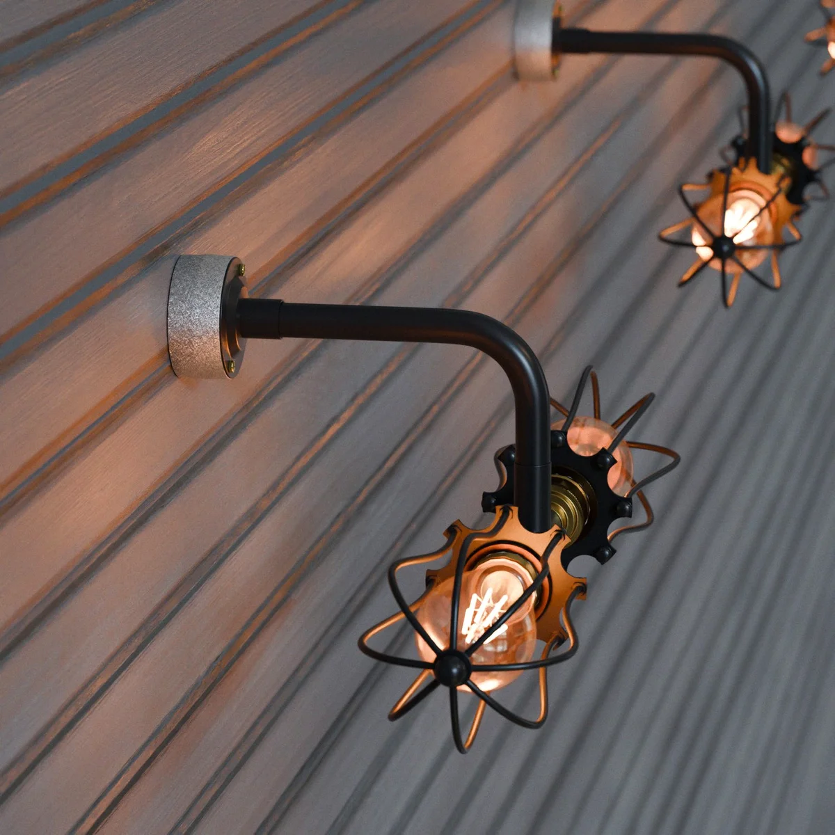 Black metal industrial wall light with two cage enclosures, vintage style, mounted on a conduit wall fixture