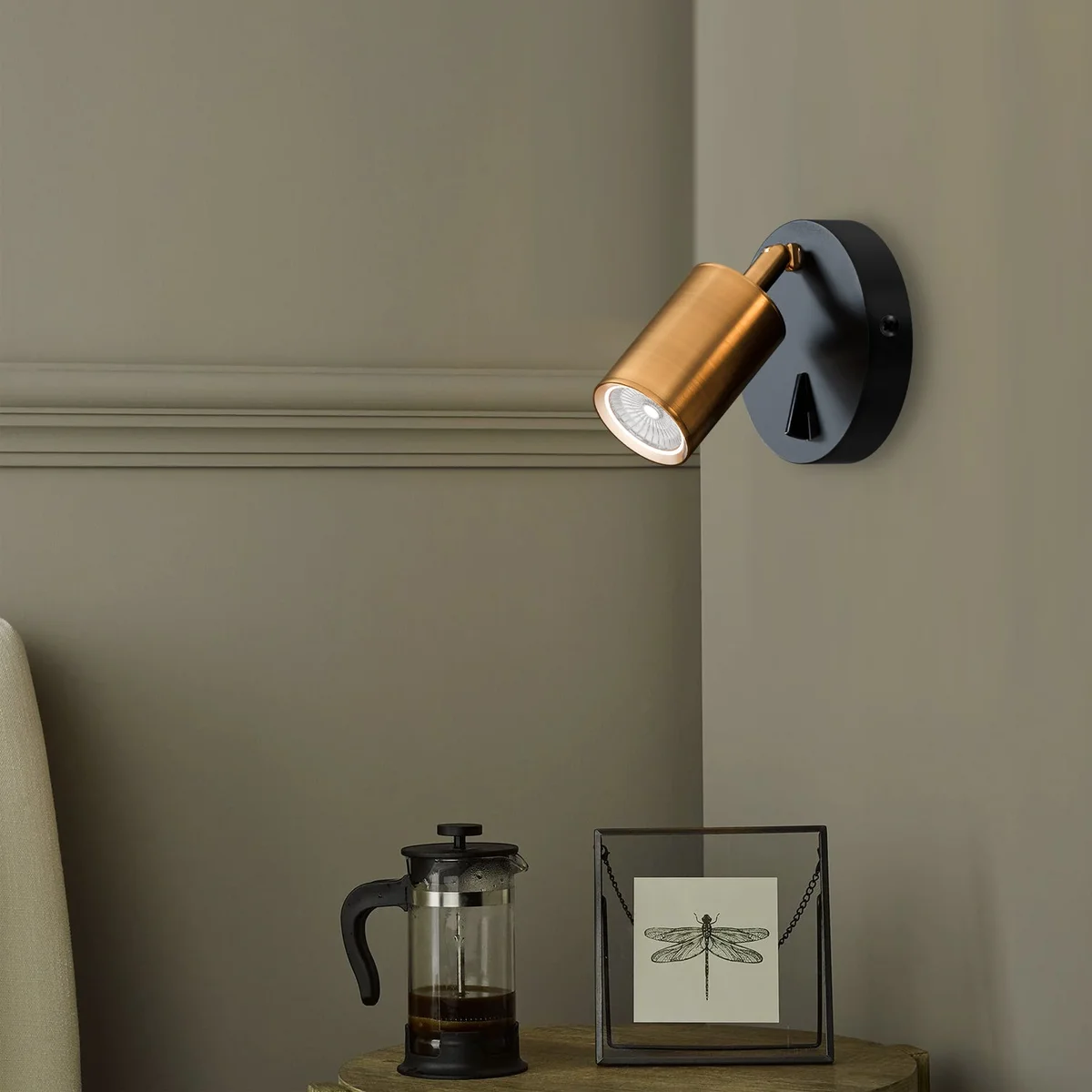 Modern wall light in yellow brass with a cylindrical adjustable spotlight and on-off switch mounted on a white wall