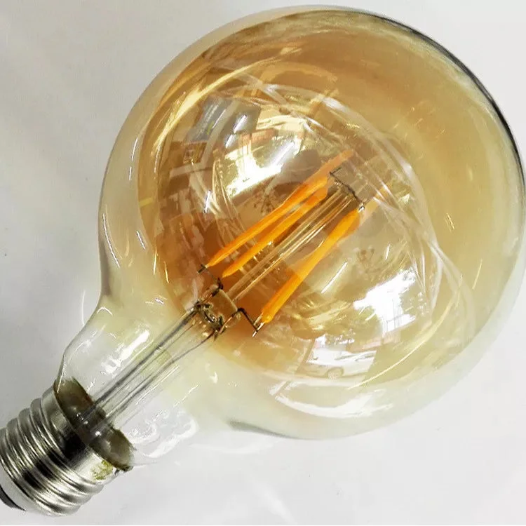 Vintage style G125 warm white LED bulb with amber glass and E27 screw base, glowing softly in dimmed light setting