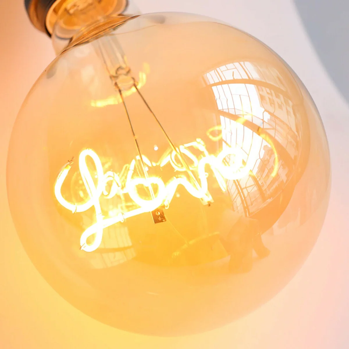 E27 LED light bulb G125 with amber glass globe and warm white curly filament glowing softly against dark background