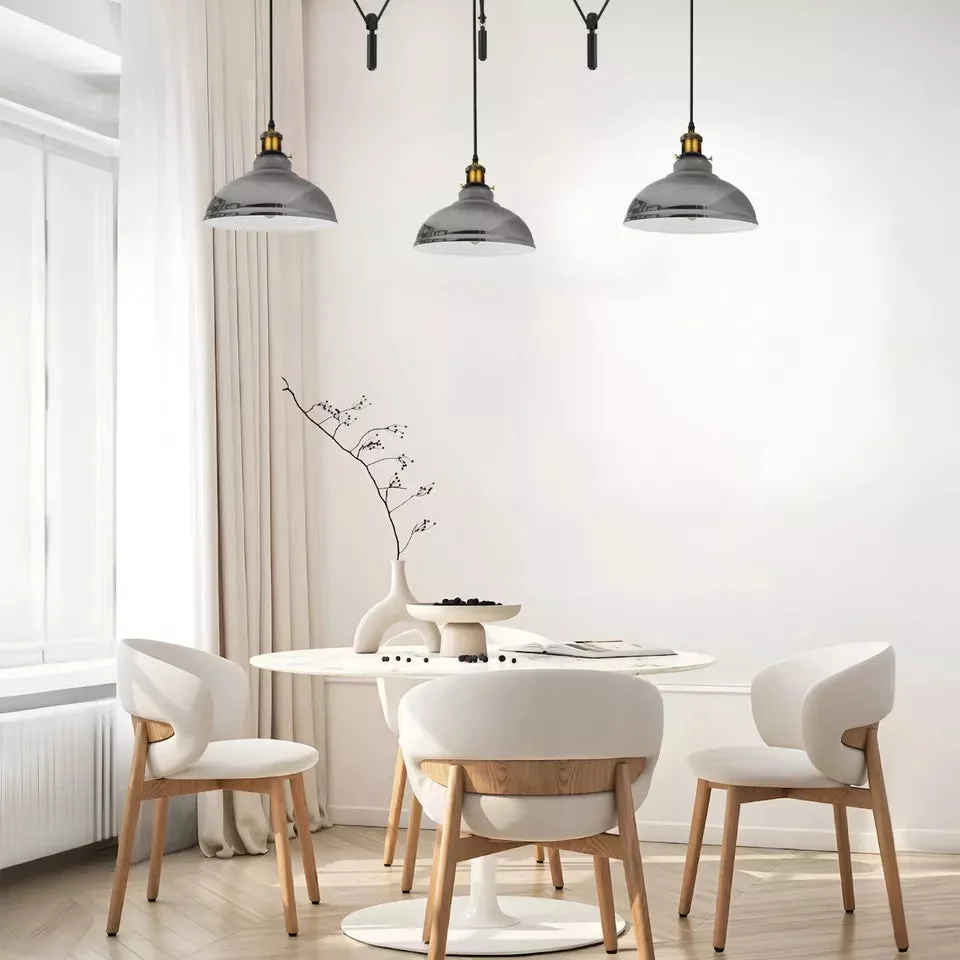 Adjustable pendant light with three metal dome shades hanging from pulleys and cords against a neutral background