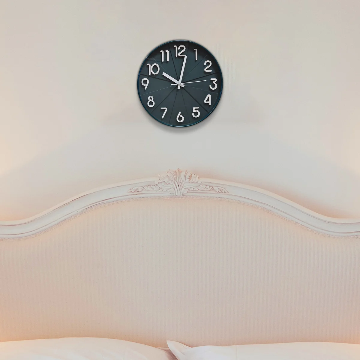 Round black silent wall clock with white numbers and hands on a black background, non-ticking, hanging on a white wall