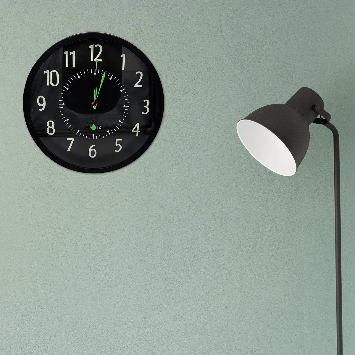 Black round wall clock with white numbers and hands on a black background, silent non-ticking design, plastic frame