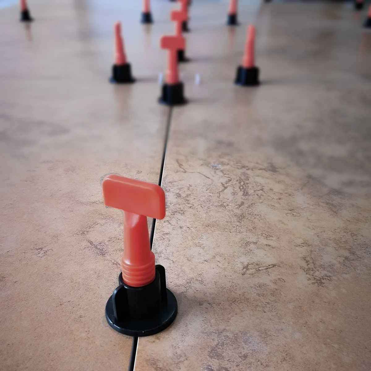 Black and red reusable tile leveling system clips with T-shaped design arranged on a white background