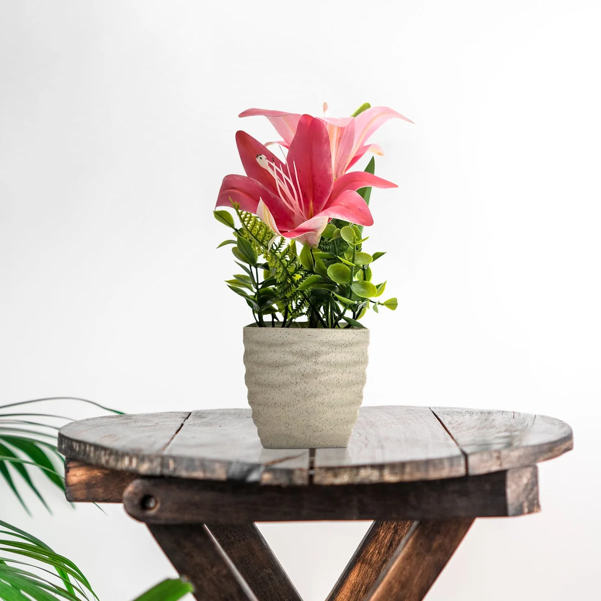 Two artificial lily flowers in white pots on a wooden table, vibrant and realistic silk blooms for decoration