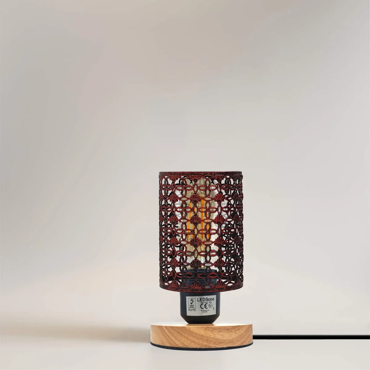 Vintage wire cage lamp with barrel-shaped metal cage and wooden stand, plugged in with visible British 3-pin plug and switch