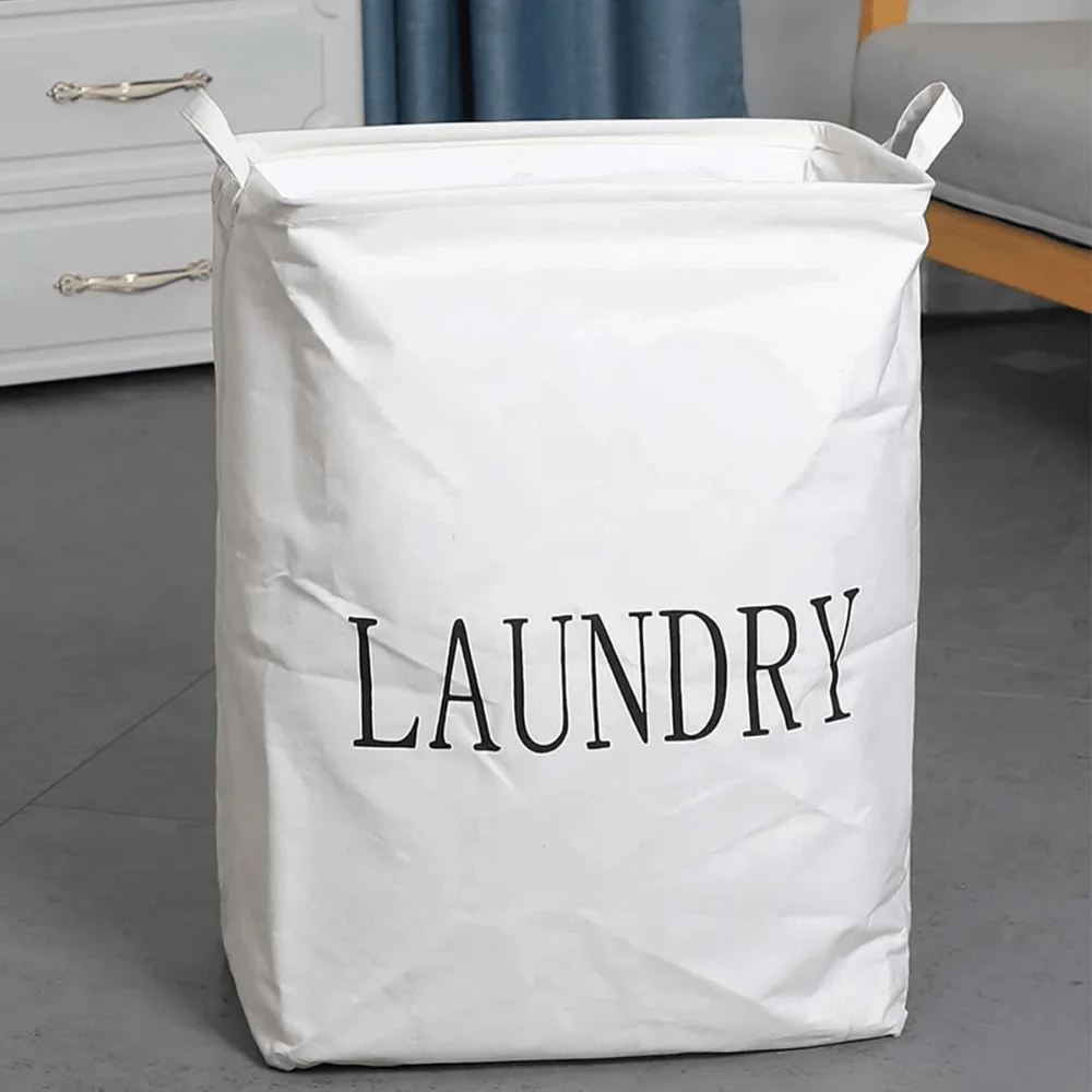 Foldable laundry bag made of cotton and linen with handles, standing freestanding in a modern bedroom setting