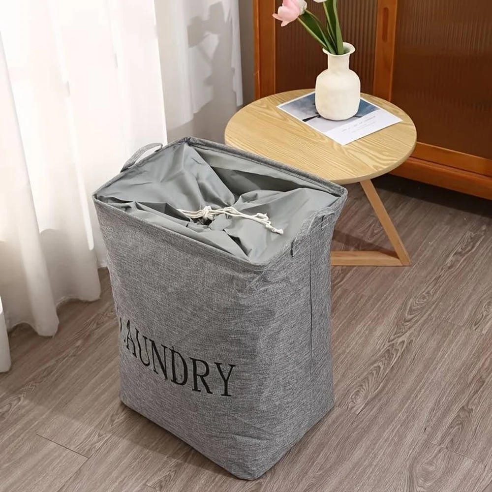 Collapsible laundry basket made of linen and cotton, square shape with handles, standing freestanding in a room corner