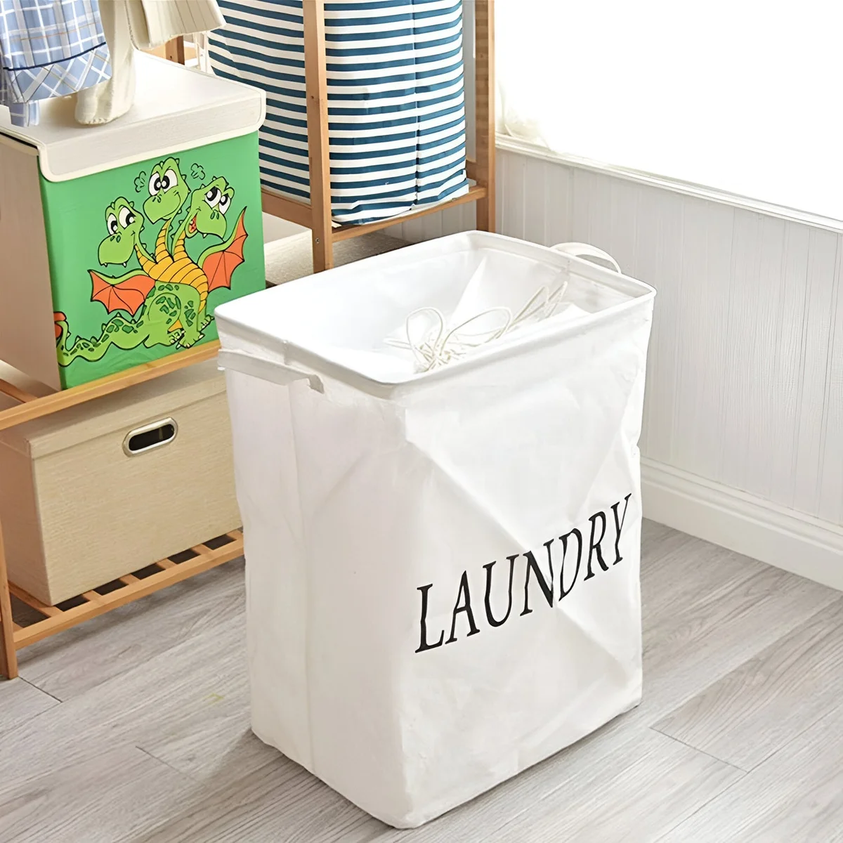 Foldable laundry bag in beige linen and cotton with handles, standing upright in a modern bedroom setting