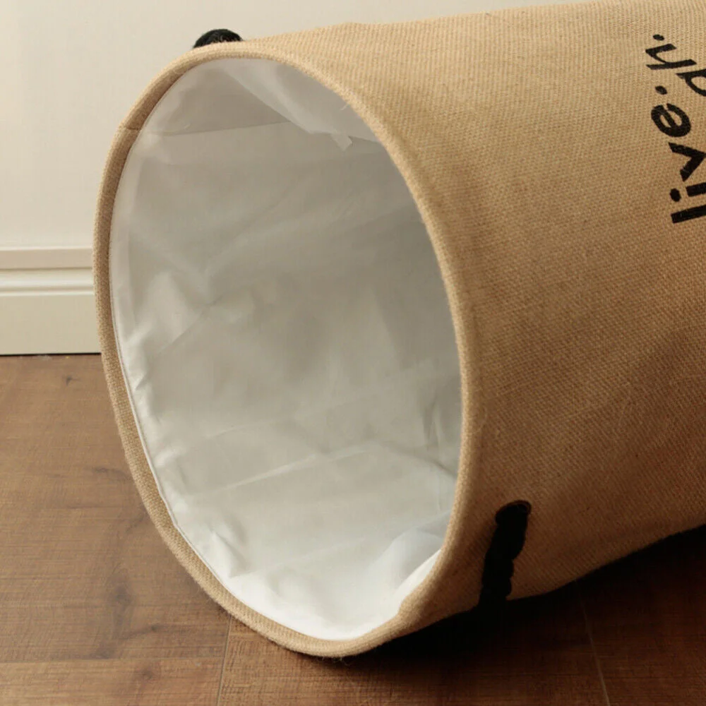 Foldable round waterproof laundry hamper made of jute with handles, standing in a bedroom corner for dirty clothes storage