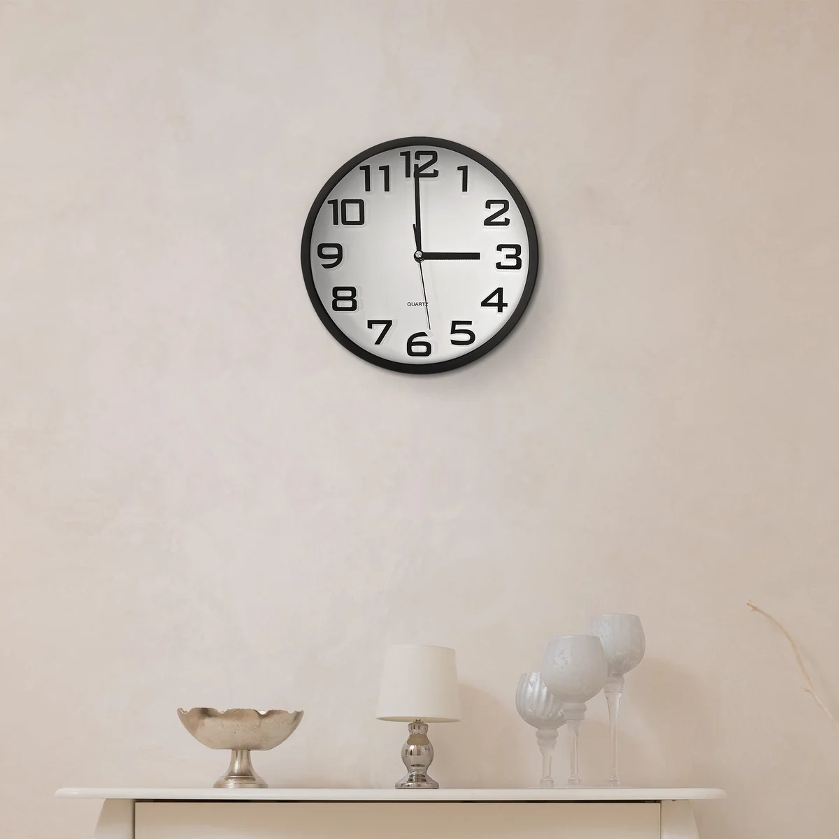 Minimalist round wall clock with white face, black numbers and hands, sleek plastic frame, hanging on white wall