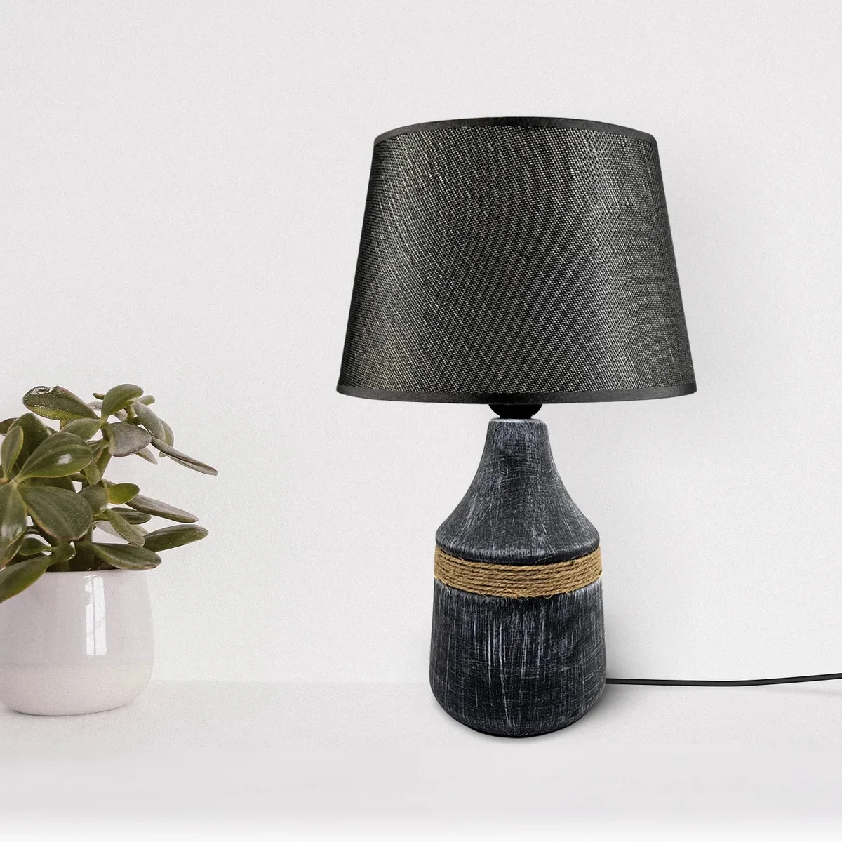 Modern minimalist bedside table lamp with black fabric shade and ceramic base on wooden surface against white wall