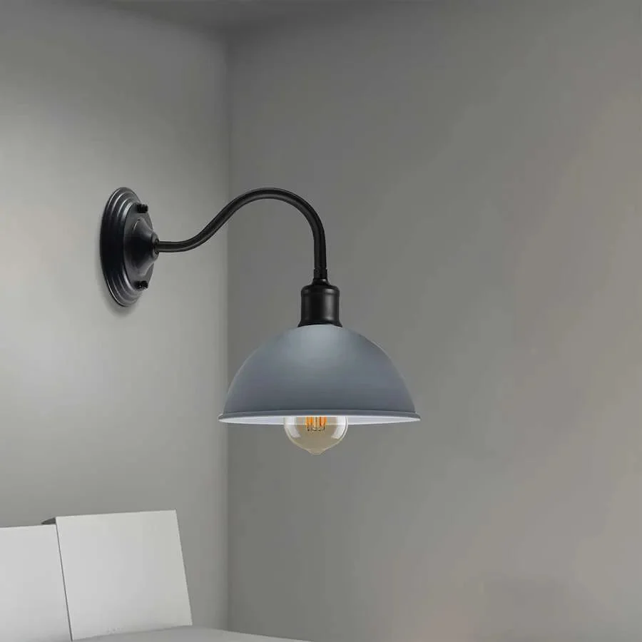 Industrial vintage style wall light with curved swan neck arm and metal dome shade mounted on a wall in a room setting
