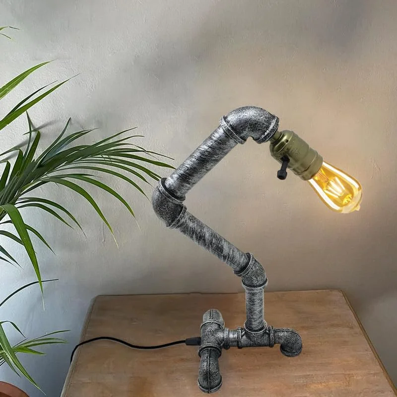 Brushed silver industrial pipe table lamp with vintage steampunk design on a wooden desk, lit with warm bulb glow