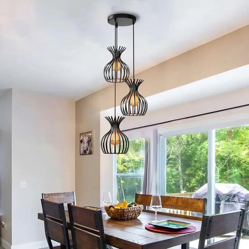 Black metal cluster pendant light with three wire cage shades hanging above dining table against white background