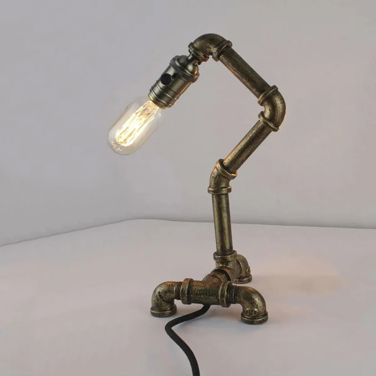 Industrial steampunk water pipe table lamp with metal pipe design and vintage-style bulb socket on wooden surface