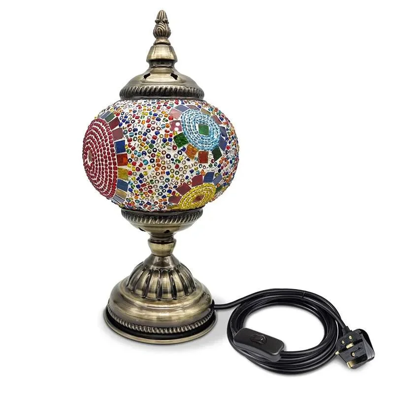Handmade glass lamp with colorful Turkish mosaic tiles and antique brass base on a wooden side table, lit softly