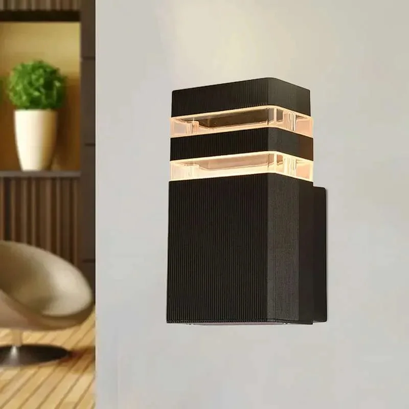 Black modern outdoor wall light mounted on a porch wall, showcasing its sleek square LED design and warm illumination