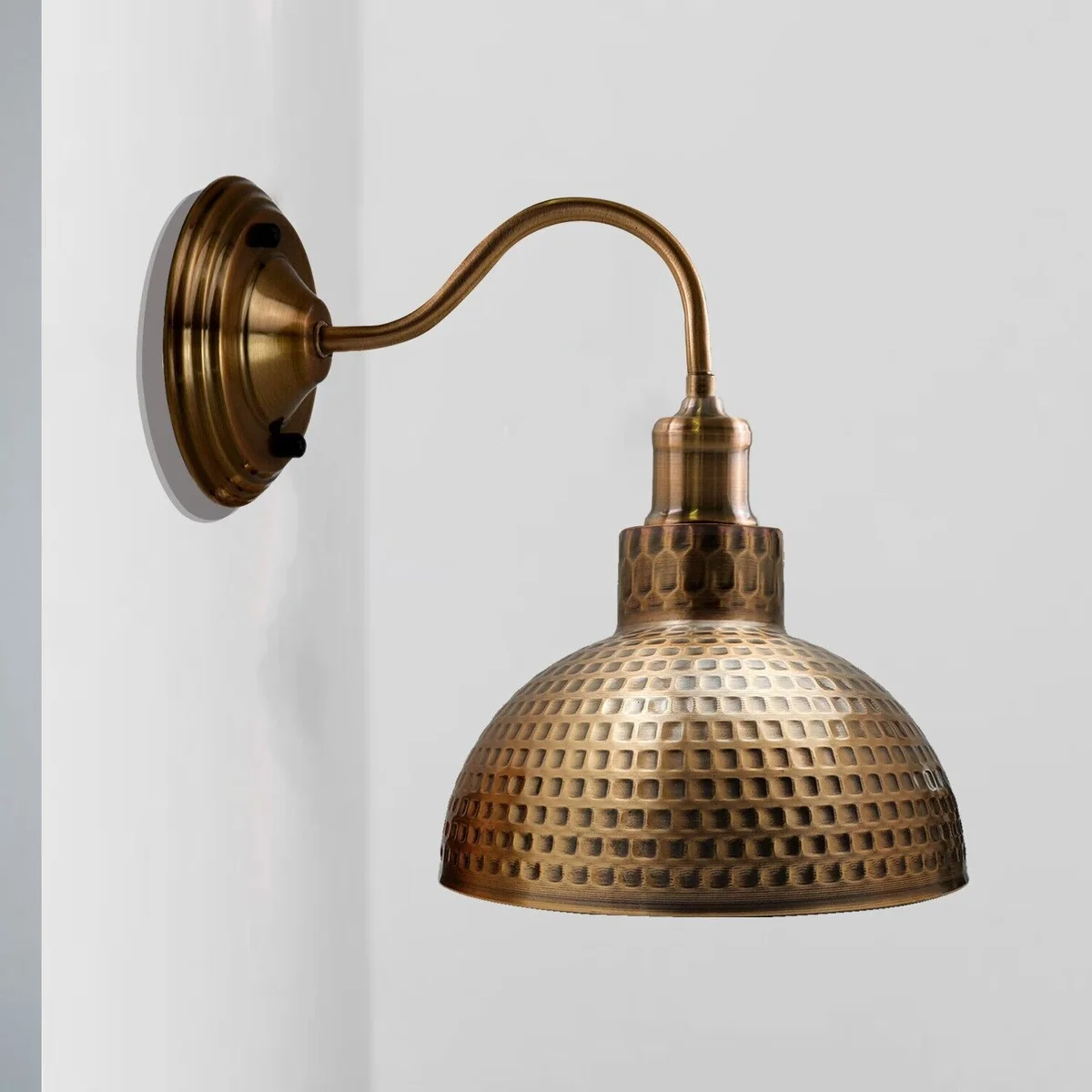 Modern rustic wall lamp with yellow brass hammered metal shade and E27 socket on wall.