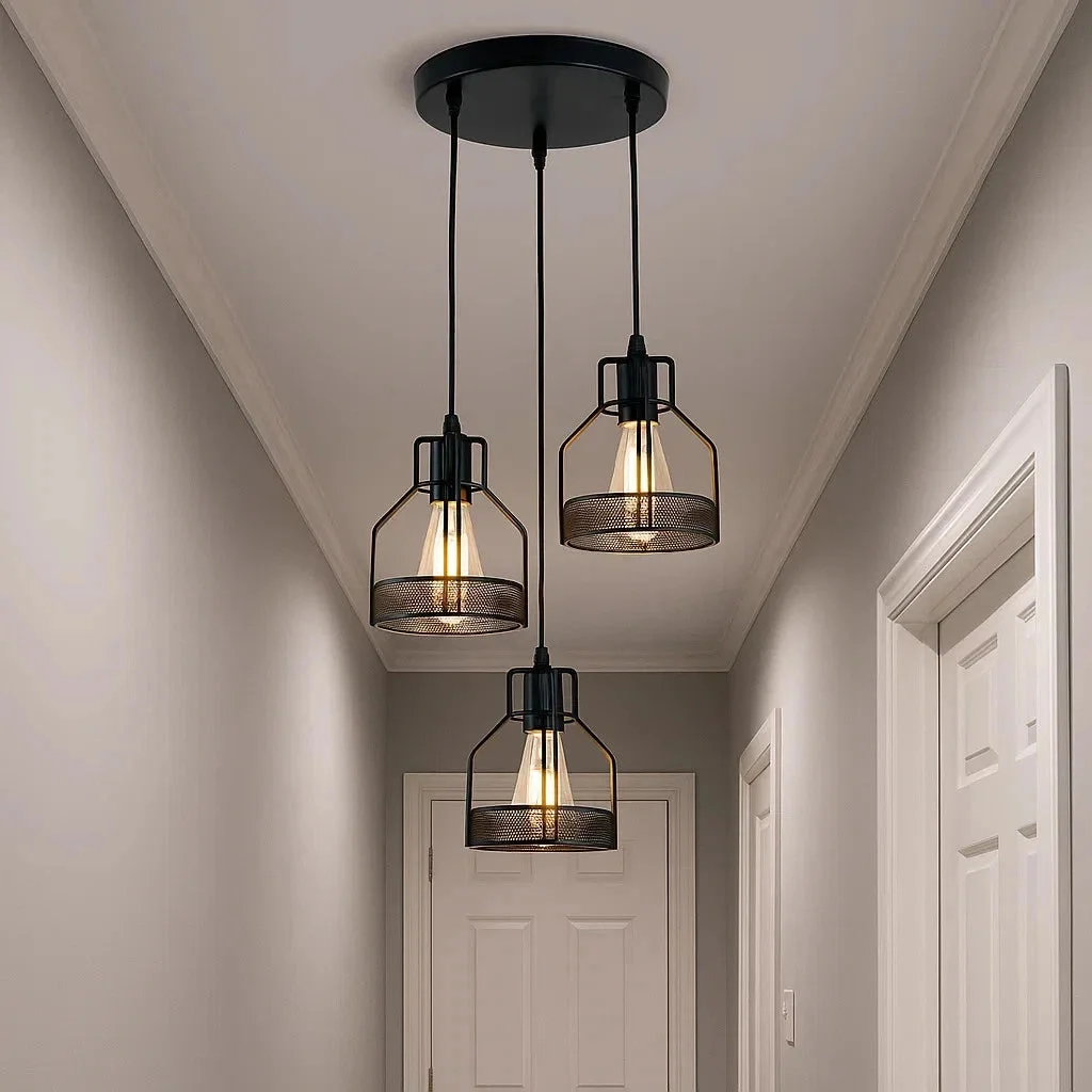 vintage industrial pendant light with 3 matte black metal arms and tinted glass shades, hung from a ceiling in a modern kitchen setting.