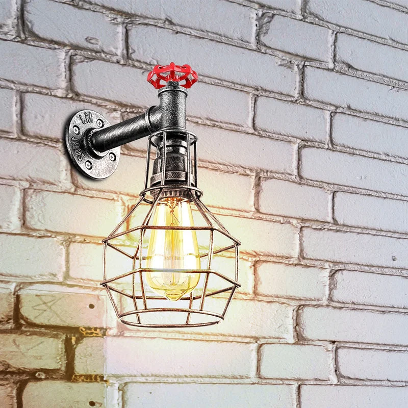 Metal cage industrial wall light with antique brass finish, glowing lamp inside, hanging on a wooden wall in a living room.