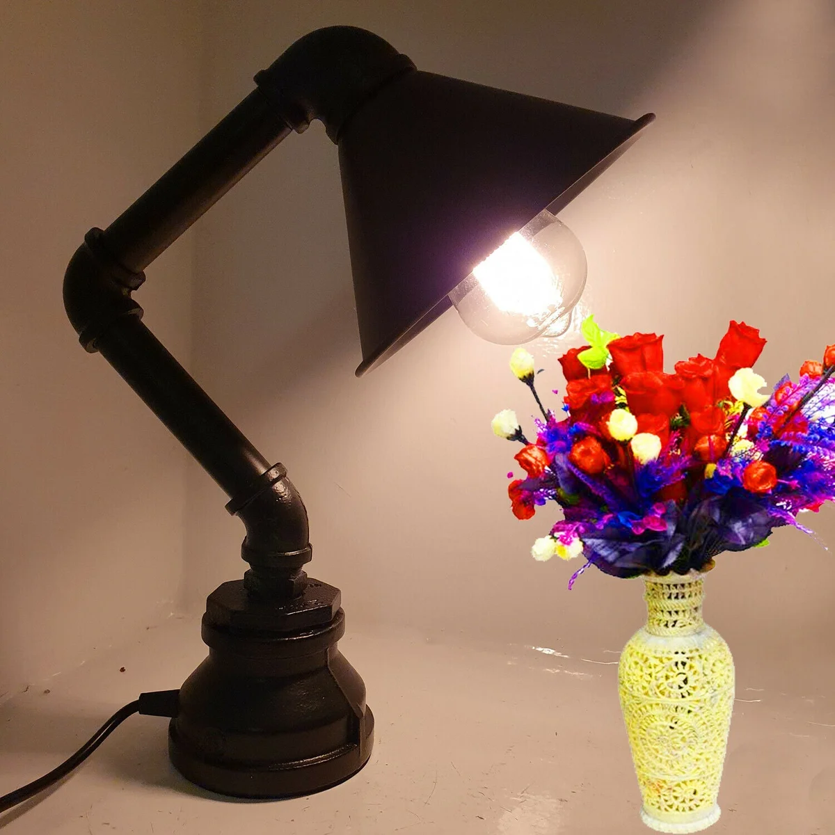 Vintage steampunk table lamp with metal water pipe design and black cone shade on wooden surface against white wall