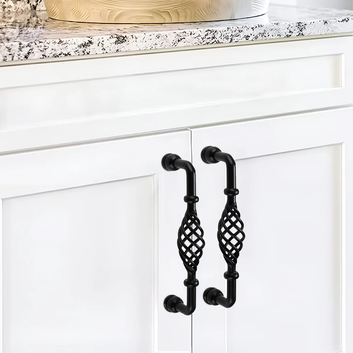 Vintage black metal cabinet handle shaped like a birdcage, shown installed on a wooden kitchen drawer front