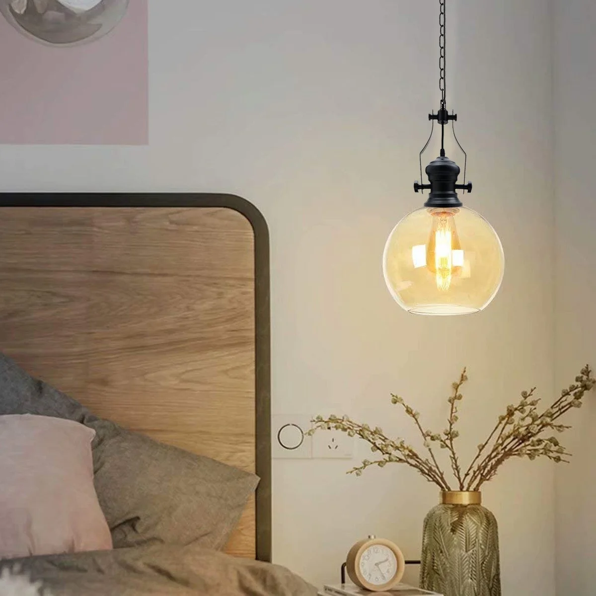 Industrial pendant light with amber glass shade and black cage suspended by chain and cable against white background