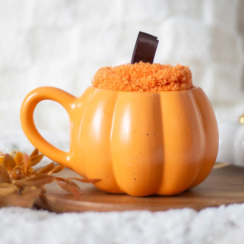 Pumpkin shaped mug with soft orange socks and brown ribbon stems, ready for a cozy autumn drink.