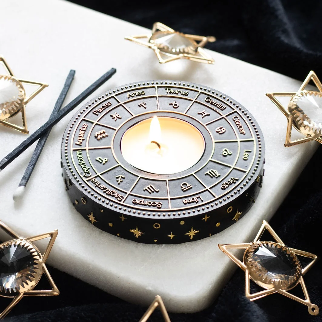 Astrology tealight candle holder with gold-effect astrology wheel design holding a lit tealight candle in the centre