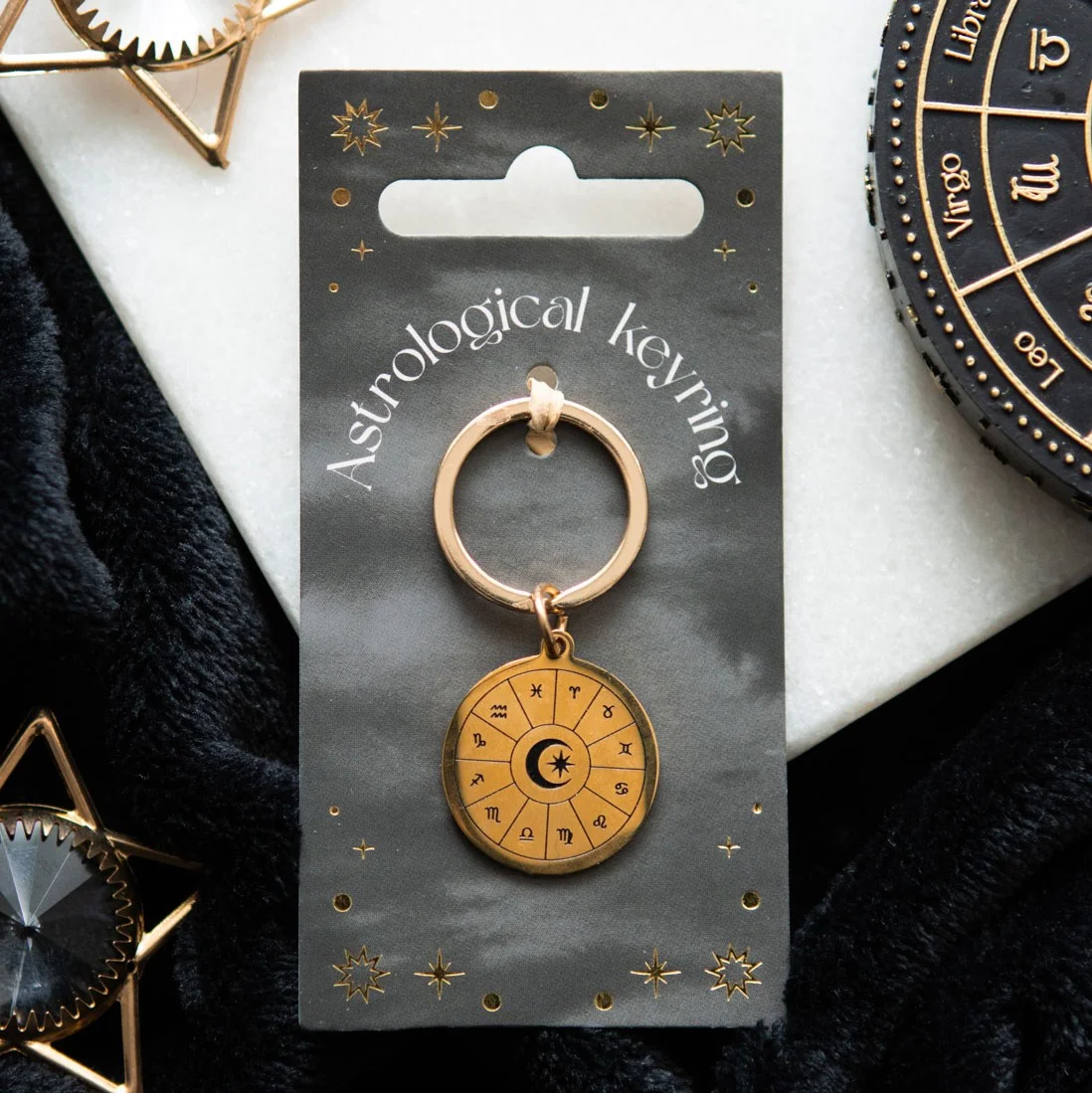 Gold tone astrology wheel keyring with detailed zodiac symbols on matching backing card against white background