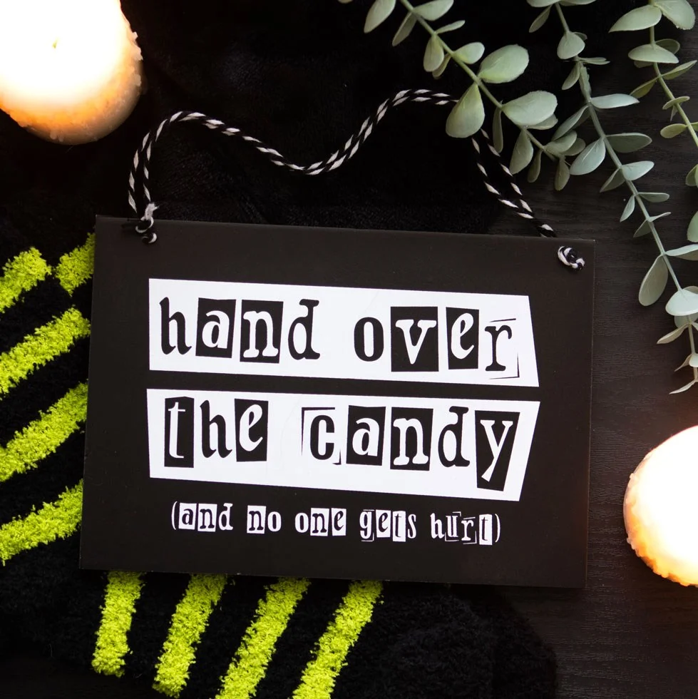 Black and white Halloween hanging sign reading Hand over the candy (and no one gets hurt) in bold text