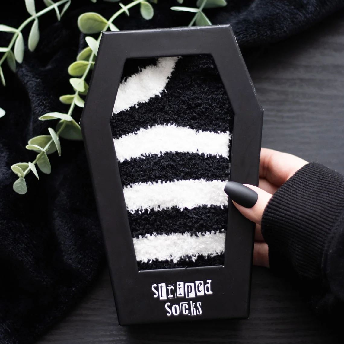 Black and white striped socks displayed inside a coffin-shaped striped socks gift box on a white background
