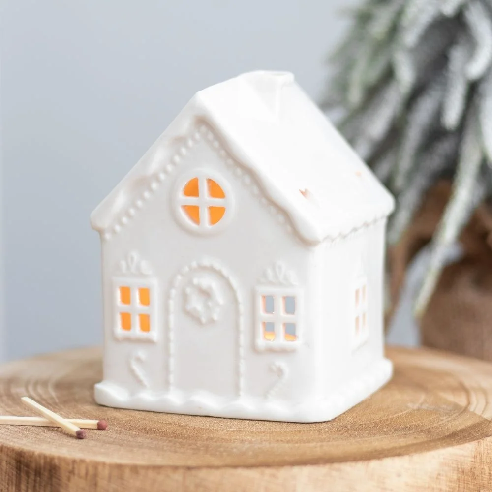 White ceramic gingerbread house tealight holder with cut-out windows, glowing softly from inside, festive winter decor