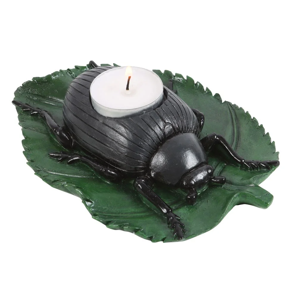 Black resin beetle tealight candle holder on a vibrant green leaf holding a single lit tealight candle