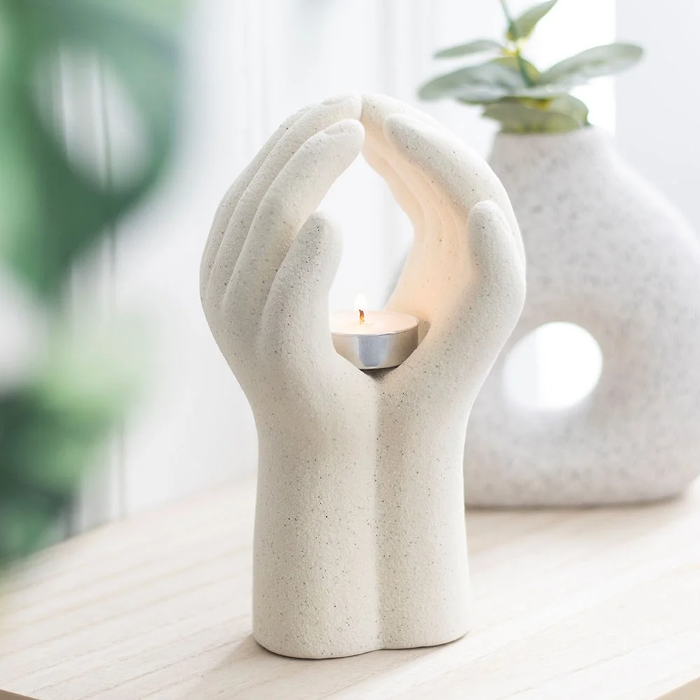 Praying hands tealight holder in modern design with lit candle casting warm glow on white background