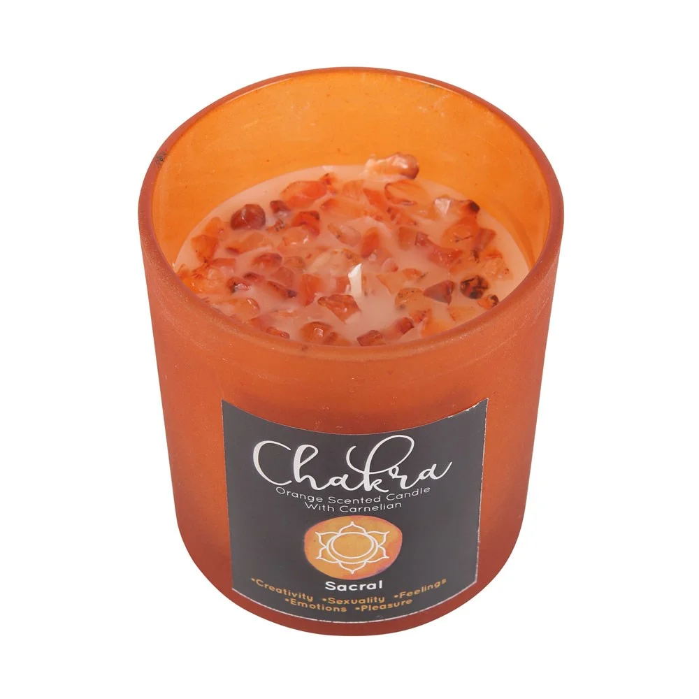 Orange frosted glass sacral chakra candle with metallic lid and scattered carnelian crystal chips on top