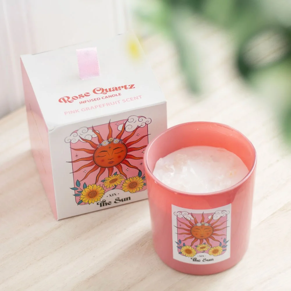 Pink glass rose quartz candle with scattered rose quartz crystal chips and lit wick on white background