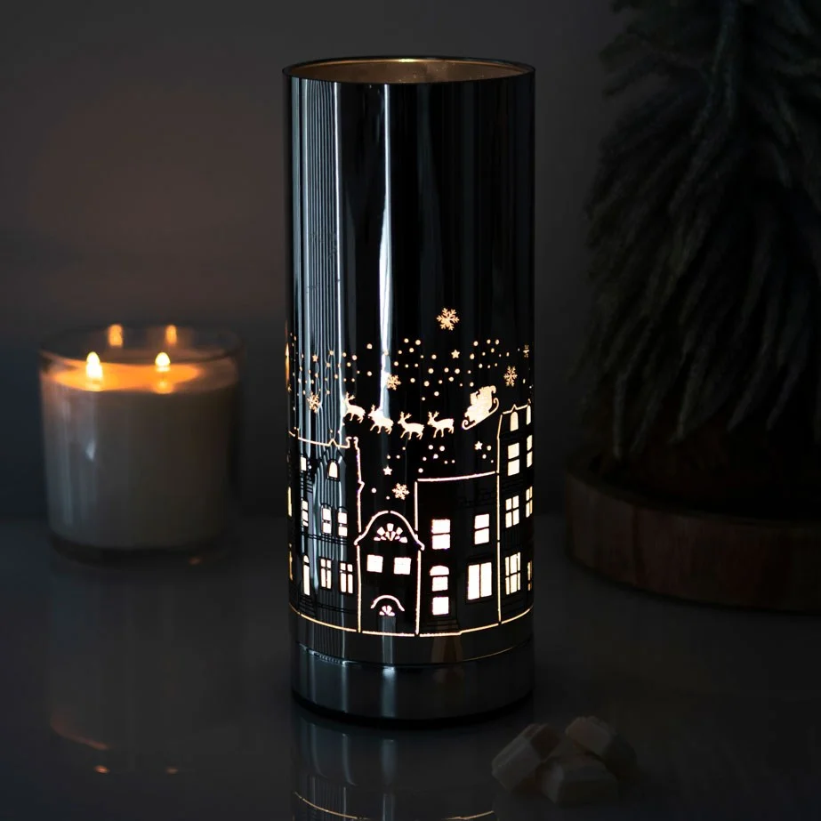 Electric aroma lamp with illuminated Christmas village design and glass dish for fragrance oils on white background